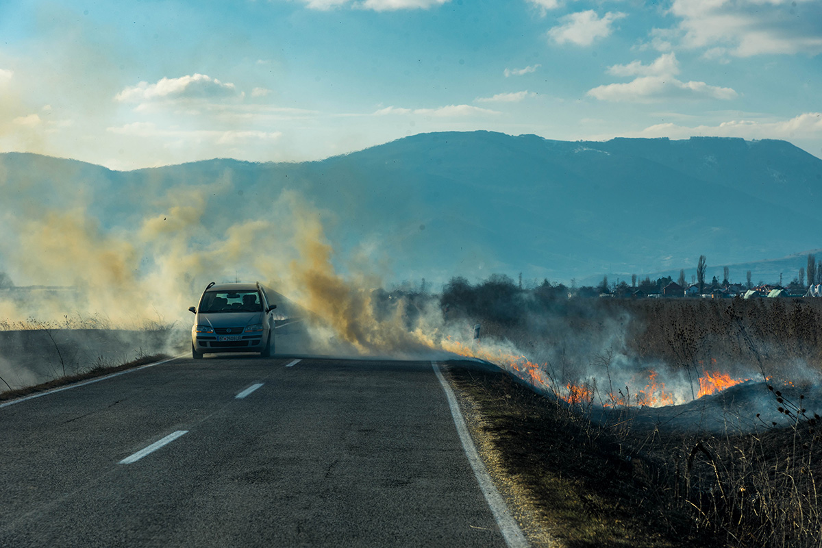 Кола која поминува на пат покрај запалено стрниште. „Палењето стрништа ја гори и почвата“